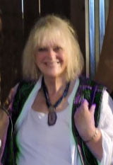 a woman with blonde hair wearing a white shirt and green vest.