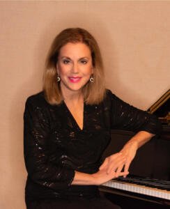 Nancy Winston sitting at a piano with a smile
