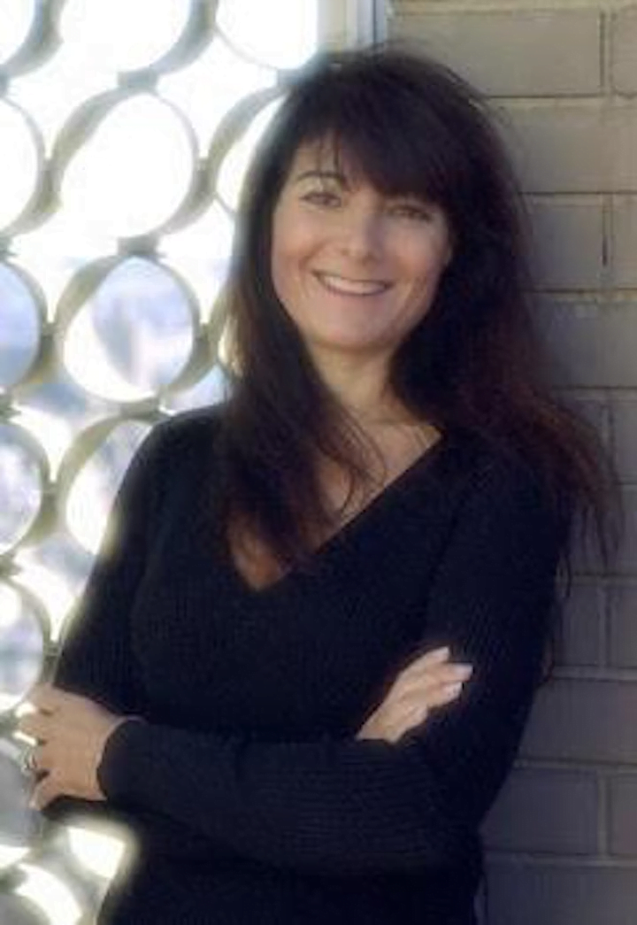 A portrait shot of Susan Shapiro in a dark long sleeve against a grated window