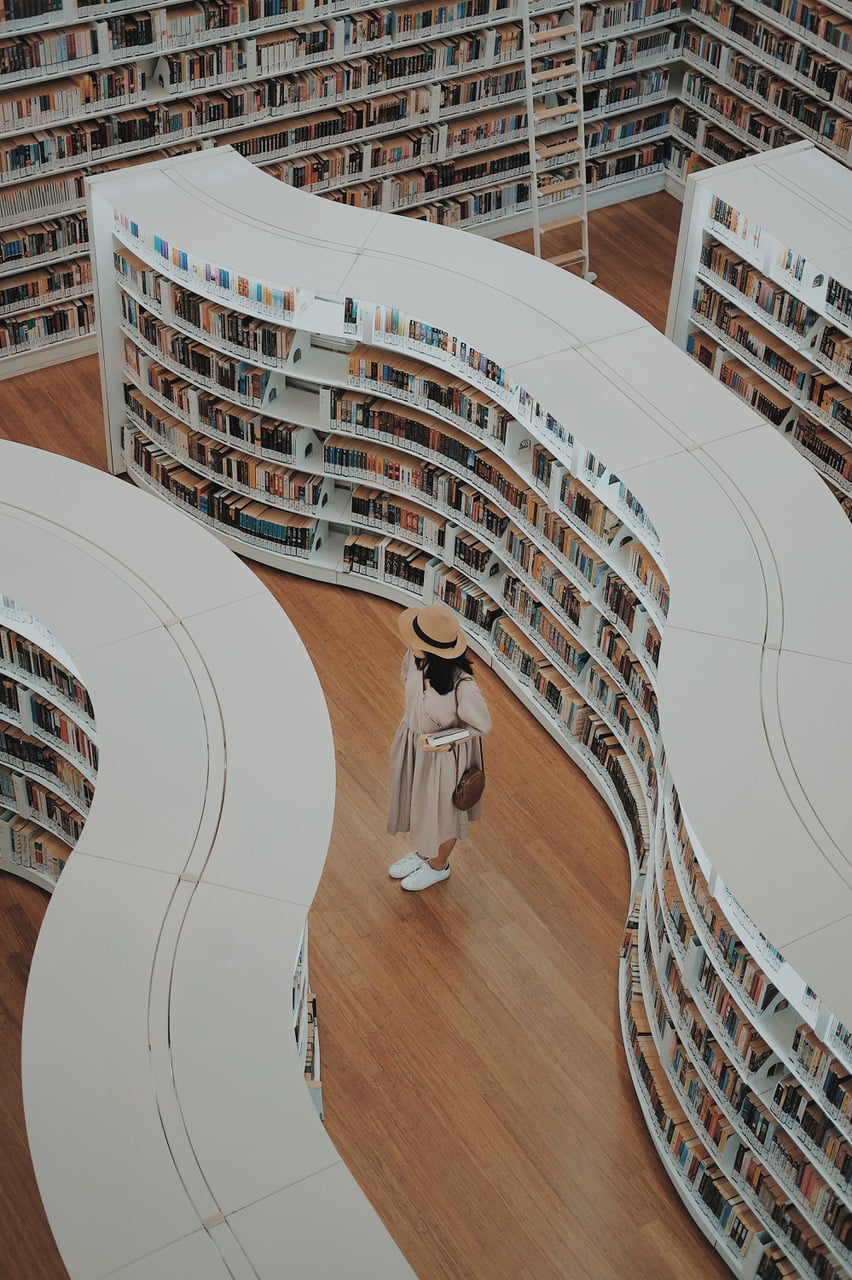 A young woman stands between aisles of curved white bookshelves