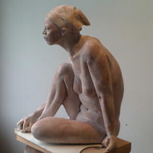 Clay-colored statue of a nude woman with a head scarf with one knee up and her hand on that side gripping her toes.