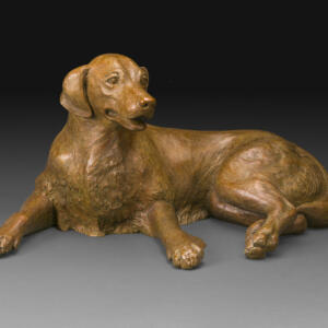 Warm brown statue of a dog laying with its back legs together and its front legs spread, and its head up.