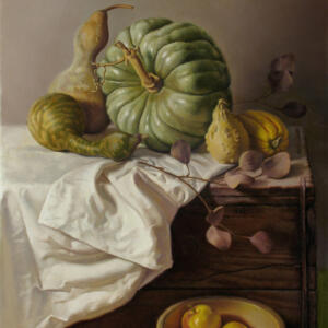 Gourds of different shapes and sizes on a table with dead branches with leaves on a wooden chest covered mostly by a white cloth, a bowl of apples out to the side.