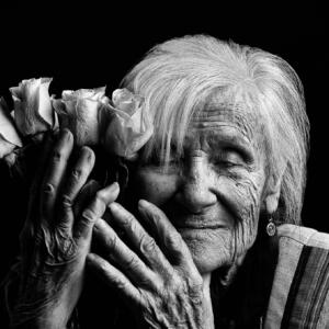 Black and white: an old woman joyfully and peacefully holds a bunch of roses to the side of her face.