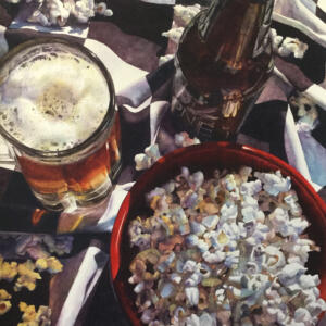 A bowl of popcorn, a beer bottle, and a glass of beer on a plaid blanket.