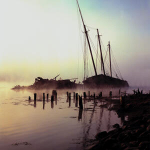 Ruins of a ship sitting on top of a body of water in the fog.
